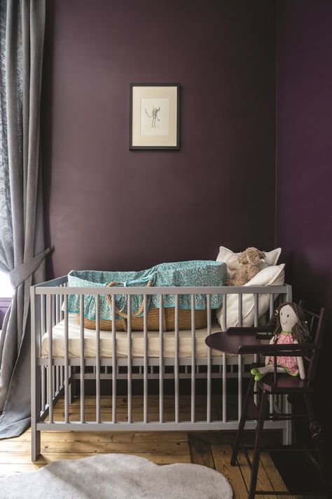 Une chambre de bébé avec des murs couleur aubergine fonce