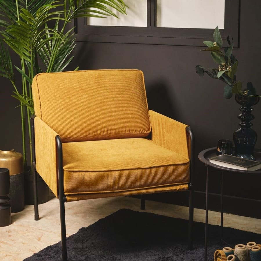 Un fauteuil jaune en velours cotele  dans un salon aux murs noirs