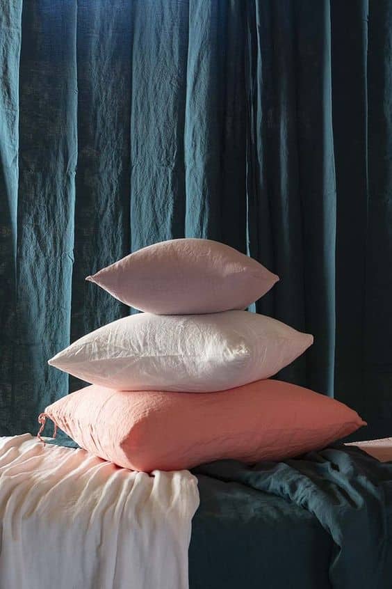 coussin en lin rose poudre dépose sur un lit devant des rideaux bleu canard