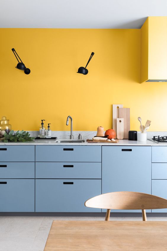Une cuisine avec un mur jaune moutarde et des meubles bleus