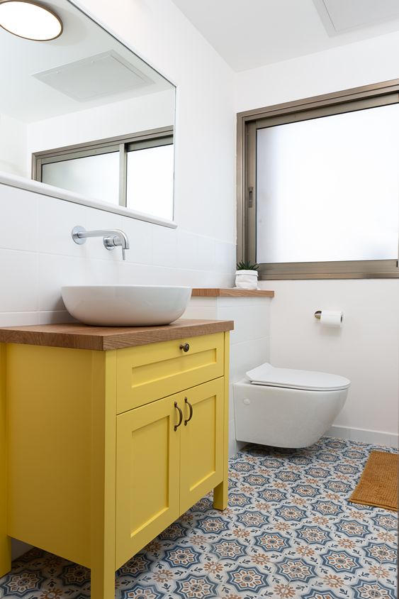 Une salle de bain blanche avec un meuble jaune moutarde et un sol en carreaux de ciment bleu et jaune