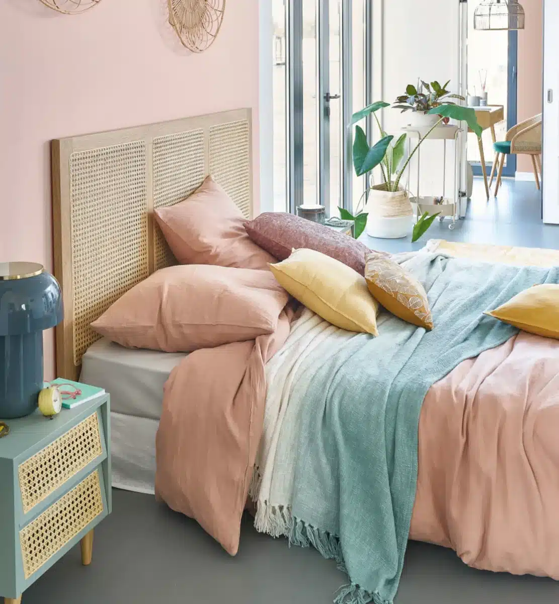 Une chambre au couleur pastel avec une tête de lit design en cannage et bois clair
