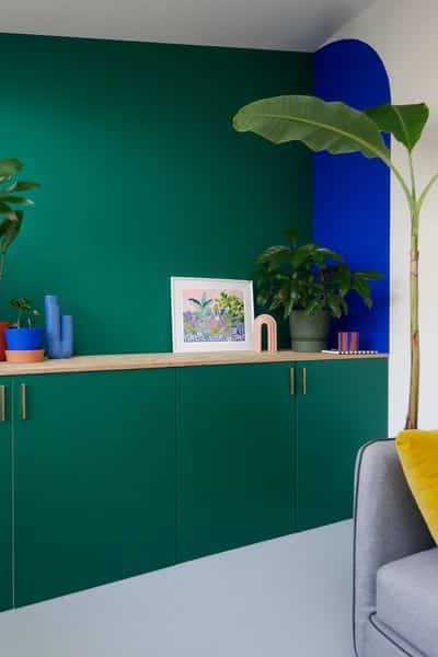 Un salon avec des rangement vert un mur vert et une forme peinte sur le mur en bleu électrique deco originale de séjour