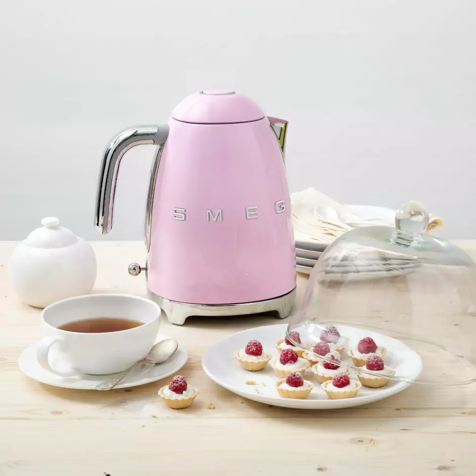 bouilloire rose smeg sur une table avec des patisserie et une tasse de the