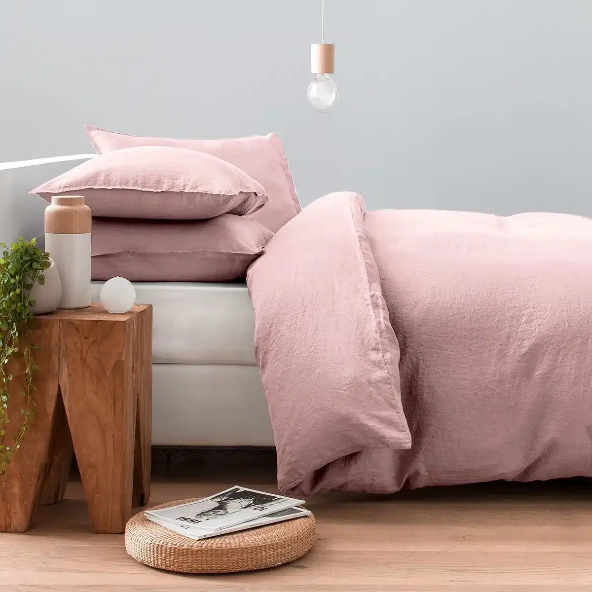 linge de lit rose dans une chambre avec parquet clair et table de chevet en bois sombre