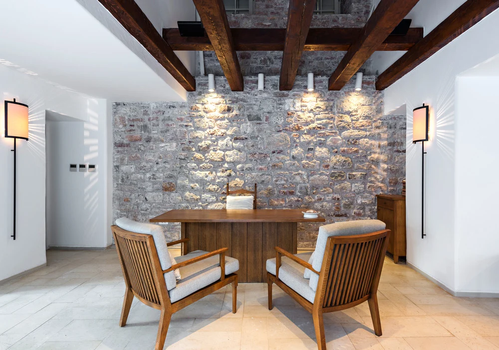 Coin repas avec un mur en pierre apparente éclairé par des appliques, poutres en bois au plafond