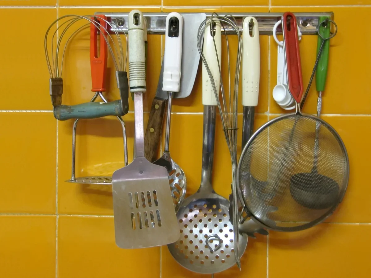 Ustensiles suspendus à une barre murale : écumoire, spatule, passoire fine, fouet
